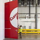 Man in safety vest opening red door to anechoic chamber in industrial setting.