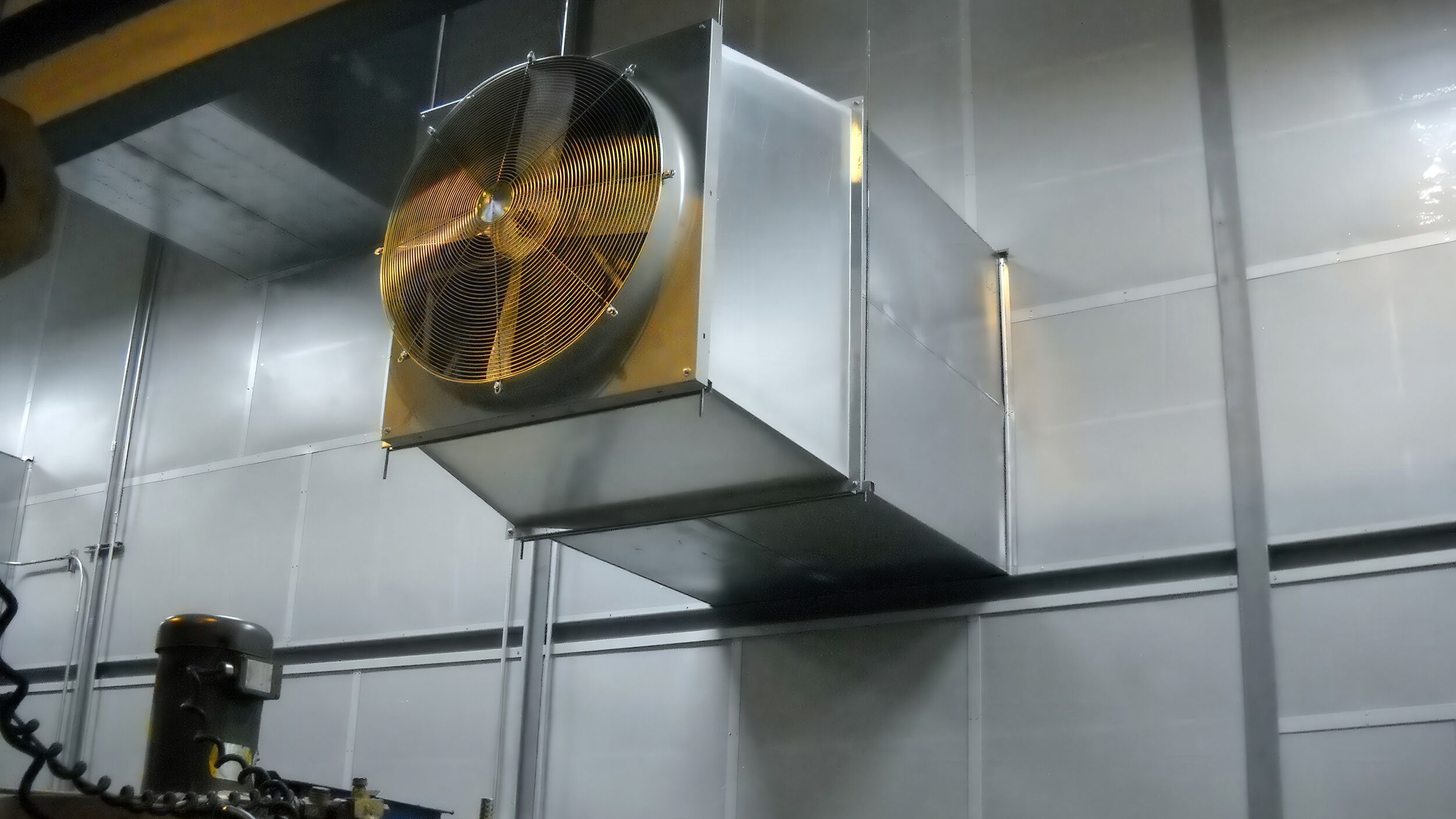 Industrial ventilation fan mounted on a metal wall in a factory setting.