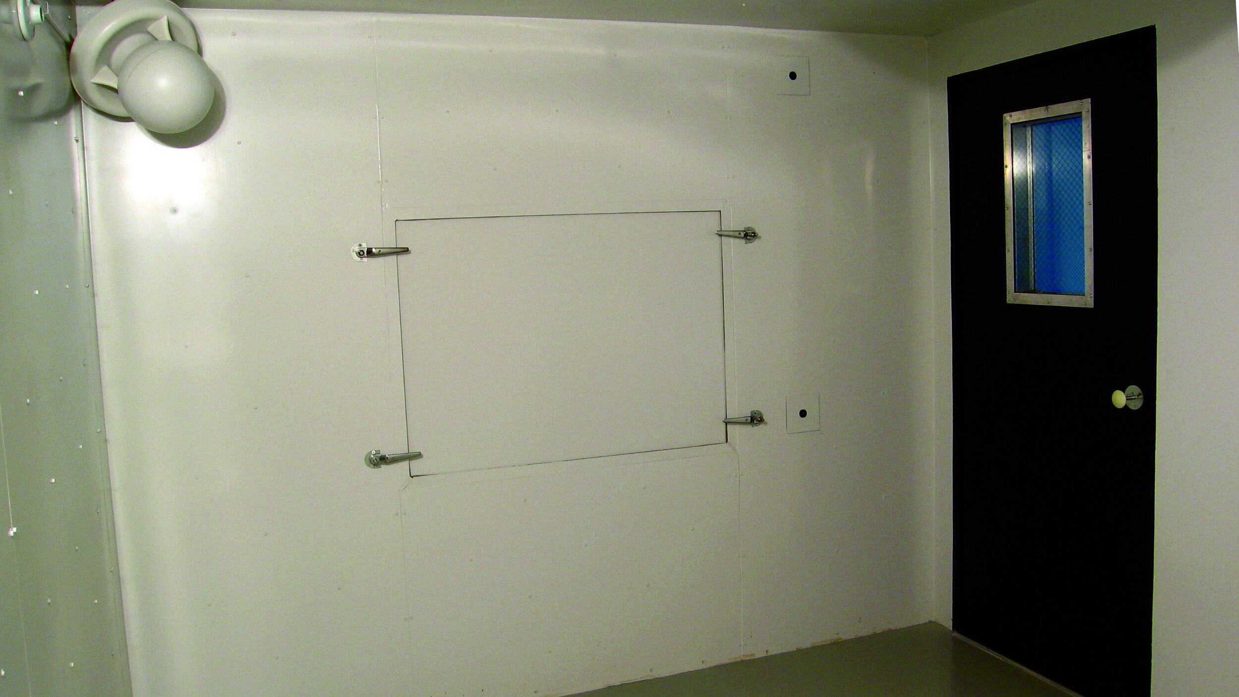Minimalistic room with a black door and ventilation features.