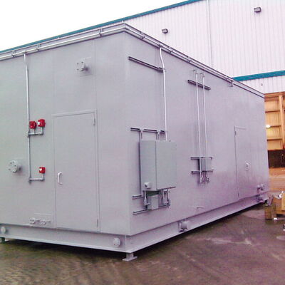 Gray electrical enclosure outside industrial building with plumbing connections.