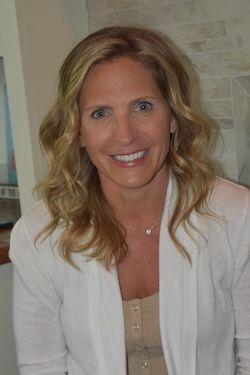 Smiling woman with wavy hair wearing a white sweater indoors.